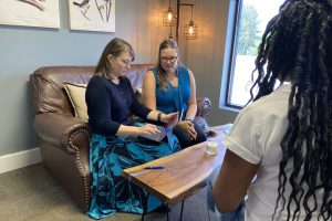 Cynthia and Tayla with a client in a cozy office discussing work while looking at a tablet near a coffee table.